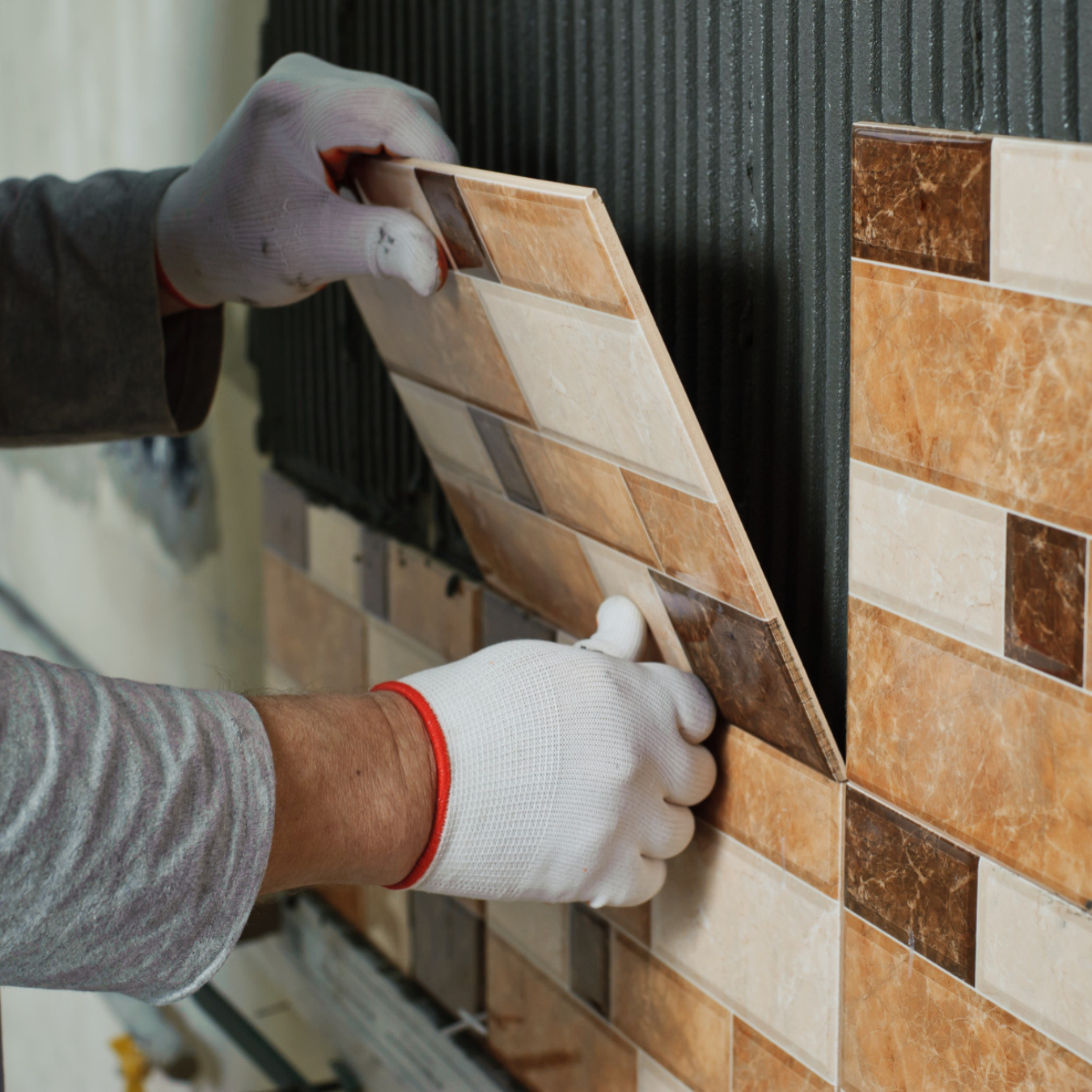 Worker installing patterned ceramic wall tiles with adhesive during home remodeling