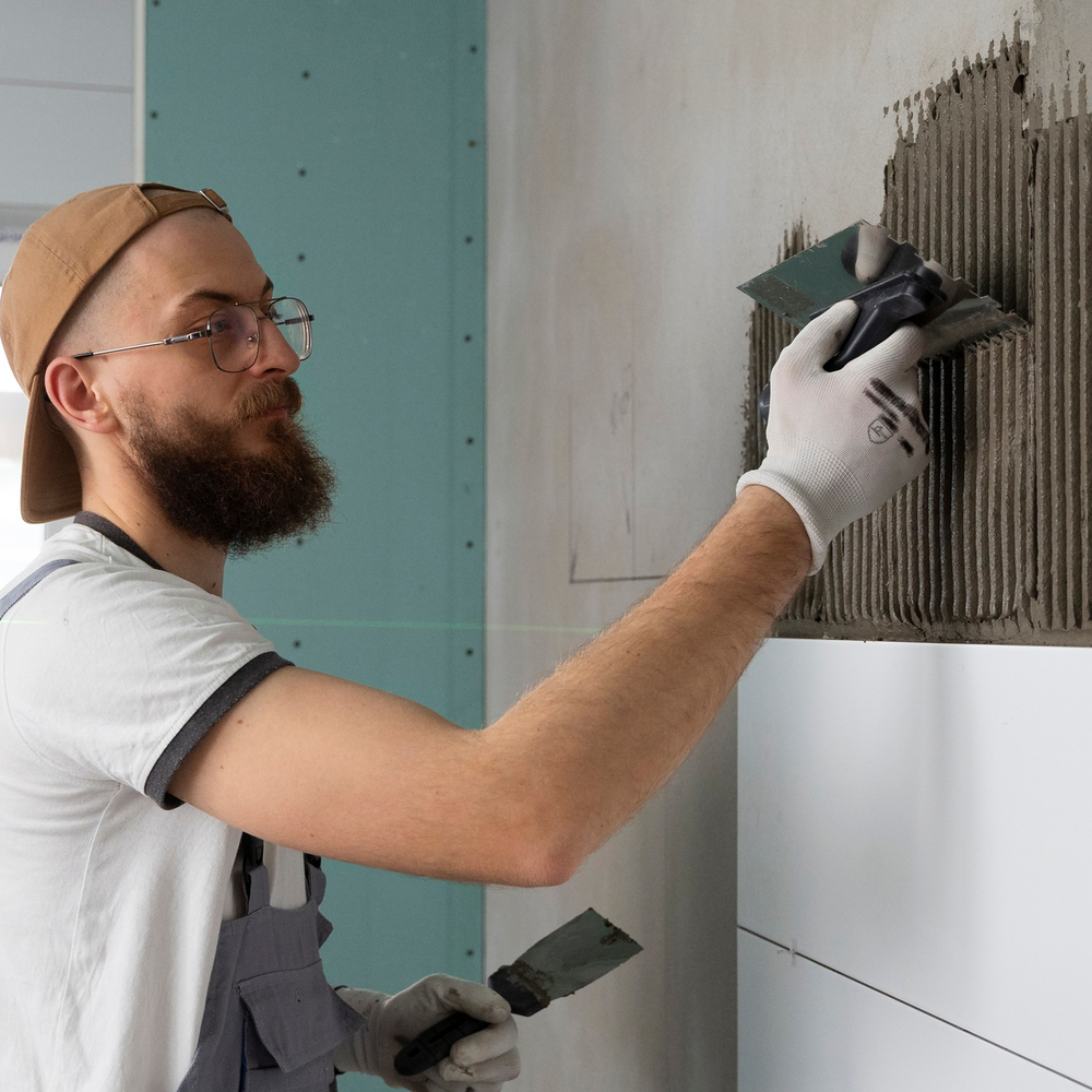 Tiling expert spreading adhesive on wall surface during installation