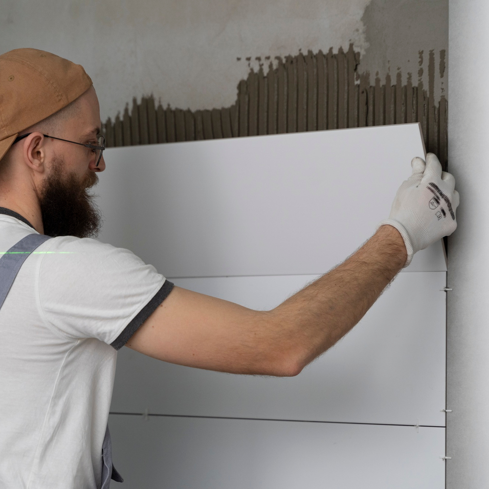 Worker installing white ceramic wall tile with spacers for alignment